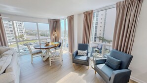 Un salon moderne avec une table ronde, deux fauteuils, un canapé et de grandes fenêtres avec des rideaux.