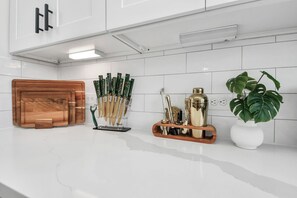 A kitchen with white tiles, a wooden cutting board, a knife holder, a gold-colored container, and a potted plant.