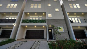 Un edificio residencial moderno de varios pisos con garaje, un pequeño jardín y fachada de ladrillo.