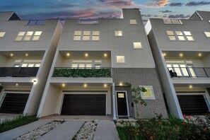 A modern multi-story residential building with a garage, a small garden area, and a brick facade.