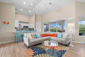 A living room with a sectional sofa, a coffee table, a dining area with a kitchen in the background, and a large window with a view. - 🏖️Private Pool Oasis | 0.2 Mi to Beach | The Oasis🏖️ (Fort Myers Beach)