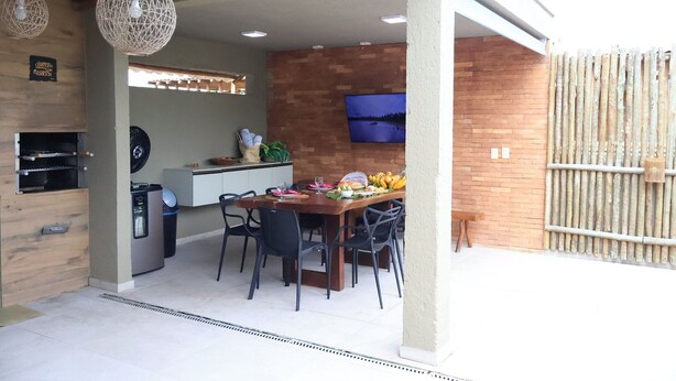 An outdoor dining area with a brick wall, a TV mounted on the wall, and a wooden ceiling.