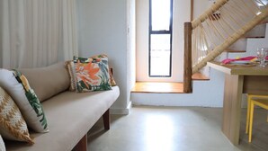 A room with a sofa, a window, a wooden staircase, and a dining table with chairs.