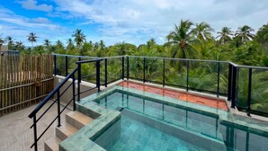 A clear view of a swimming pool with a glass barrier, surrounded by a wooden fence and palm trees.