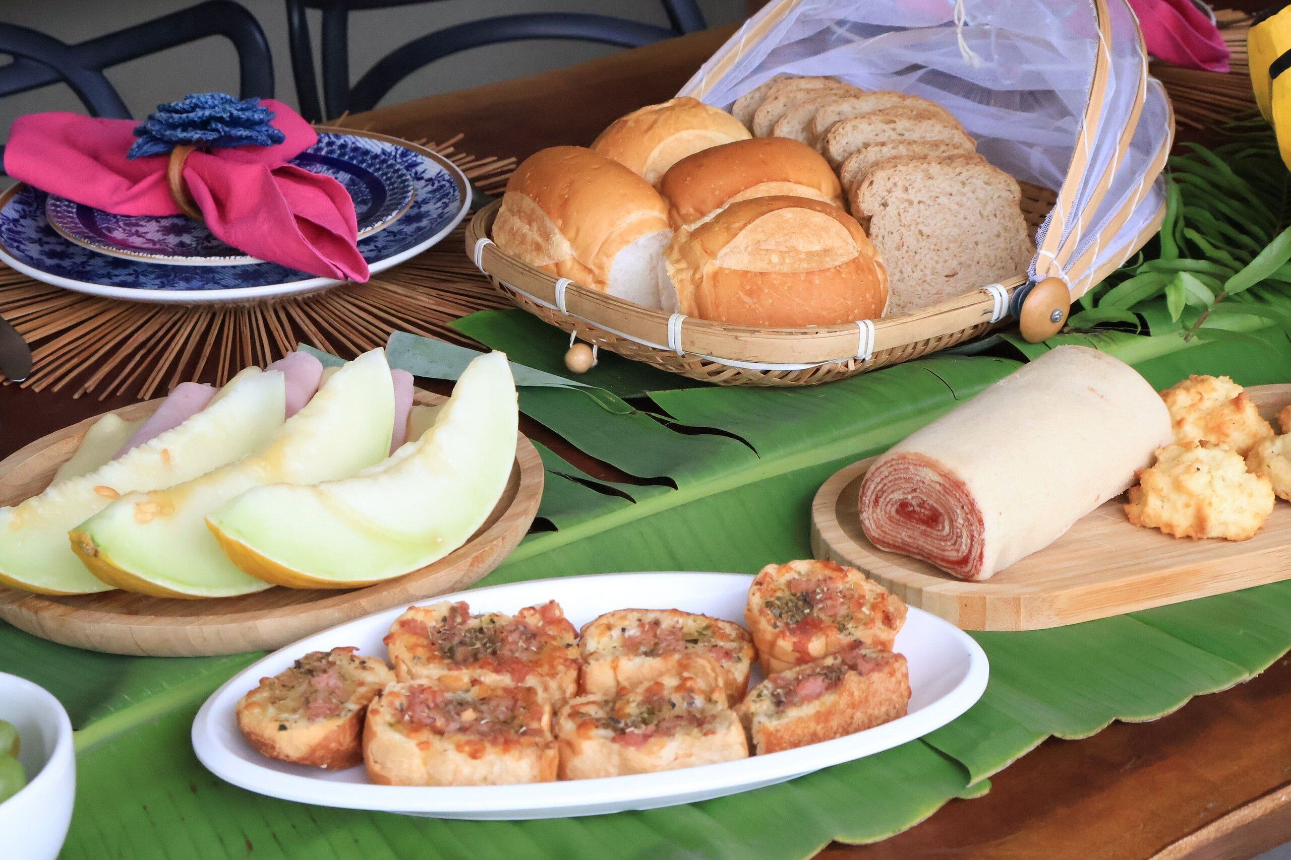 A table with various food items, including bread, rolls, and a plate of sliced apples.