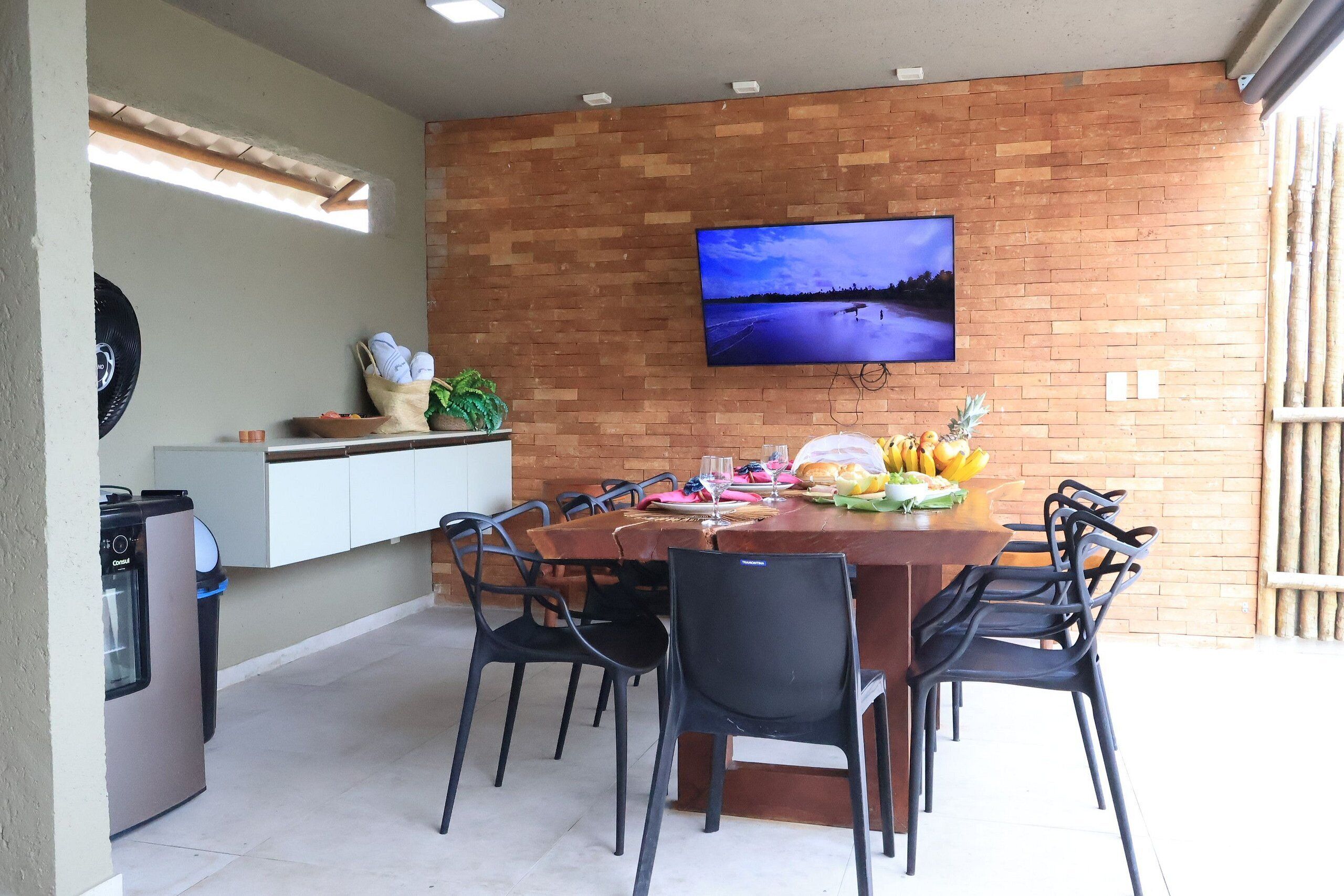 Un coin repas avec un mur en briques, un téléviseur à écran plat et une table dressée pour six personnes.