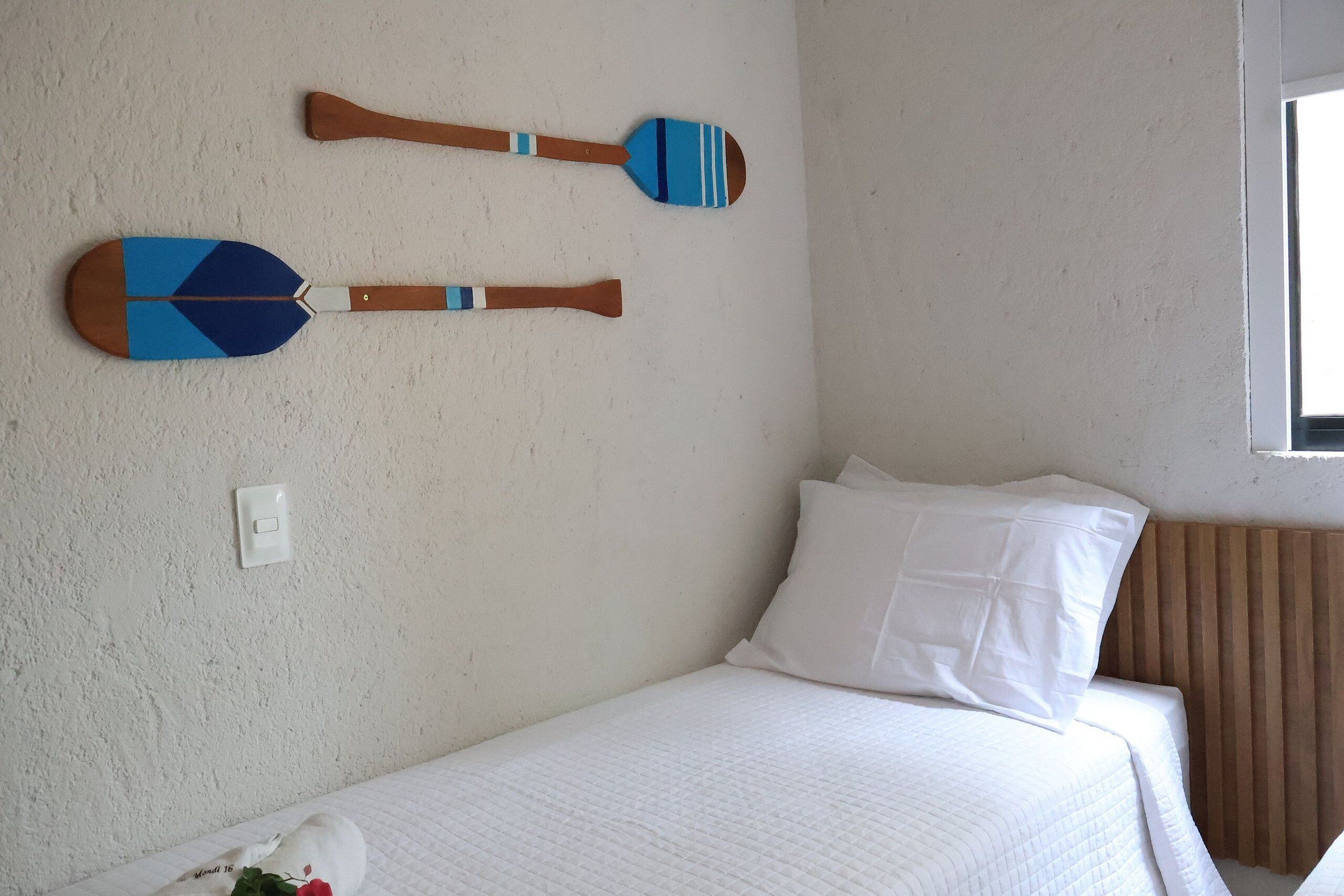 Quarto de hotel com cama, almofadas, interruptor de luz fixado na parede e dois remo de madeira na parede.