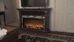 Ein Kamin mit Fernseher darüber, ein gemustertes Teppich und eine hölzerne Bank.
