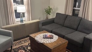 Ein Wohnzimmer mit einer Couch, einem Holztisch, einem Teppich mit Muster und einer Heizung.