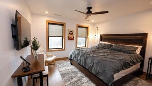 A bedroom with a bed, a desk, a chair, a ceiling fan, and two windows. - Cozy well-appointed Guest Suite on a grass airstrip (Hanover)