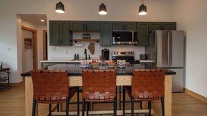 A modern kitchen with green cabinets, a stainless steel refrigerator, a microwave, and a coffee maker. There are three woven chairs at the island. - Cozy well-appointed Guest Suite on a grass airstrip (Hanover)