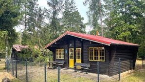 Eine Blockhütte mit rotem Dach, einem eingezäunten Garten und einem Picknicktisch.