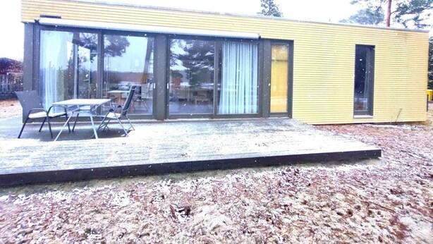 Ein modernes Gebäude mit großen Glasfenstern, einem Flachdach und einer Terrasse mit Gartenmöbeln.