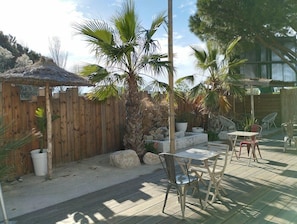 A patio with a wooden fence, palm trees, a thatched-roof structure, and outdoor seating. - Campanile Arles (Arles)