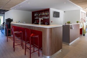 Un espace bar moderne avec un comptoir en bois, des tabourets de bar rouges et un téléviseur fixé au mur.