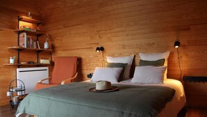 Une chambre confortable avec un plafond en bois, un lit agrémenté de plusieurs oreillers, une chaise, un bureau et des étagères remplies de livres et d’objets décoratifs.