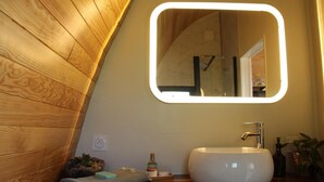 Une salle de bain avec un mur en bois, un lavabo blanc, un miroir avec un éclairage intégré et une serviette posée sur le comptoir.