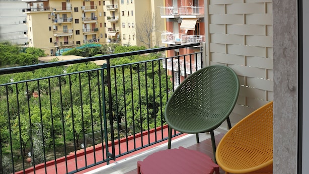 A balcony with a view of a residential building, a green chair, a red chair, and a yellow chair. - francescosuite b&b (Sorrento)