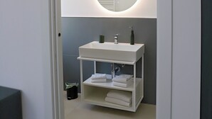 A bathroom with a round mirror, white sink, and shelves with towels. - francescosuite b&b (Sorrento)