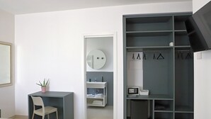 A modern bedroom with a bed, a desk, a chair, a small potted plant, a mirror, a wardrobe, and a microwave. - francescosuite b&b (Sorrento)