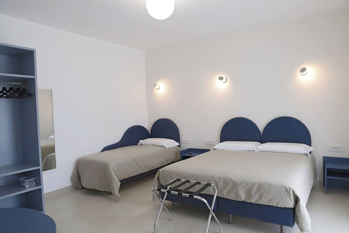 Habitación de hotel con dos camas, un armario, un espejo y una mesita de noche.