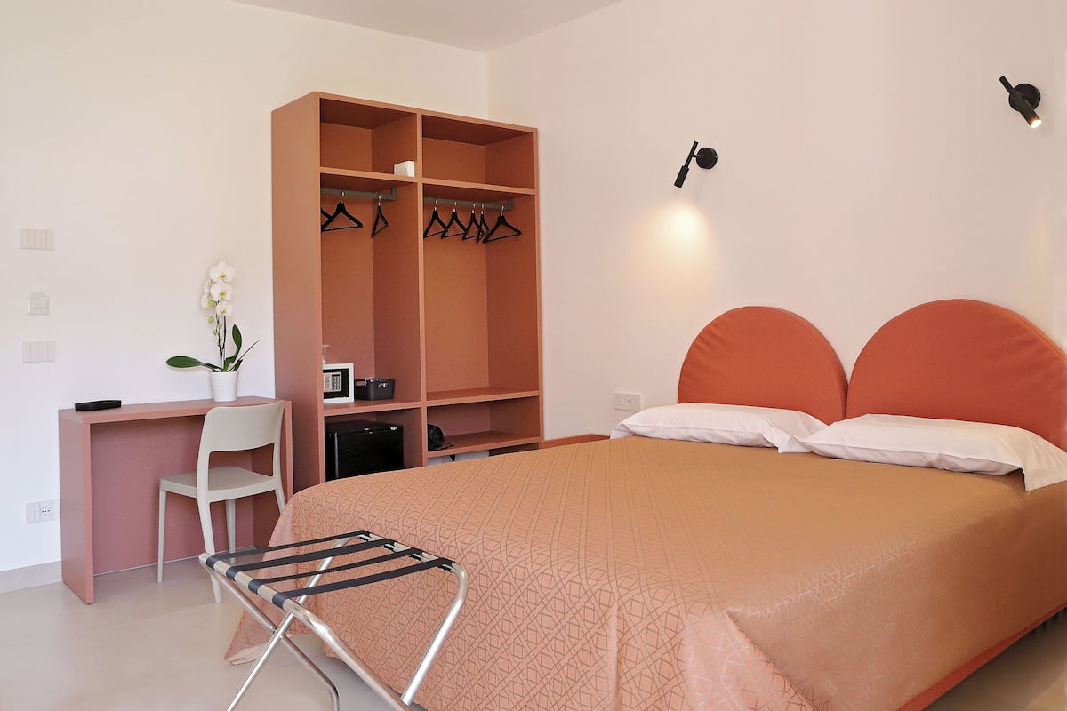 Un dormitorio con cama, escritorio, silla, armario e iluminación en la pared.