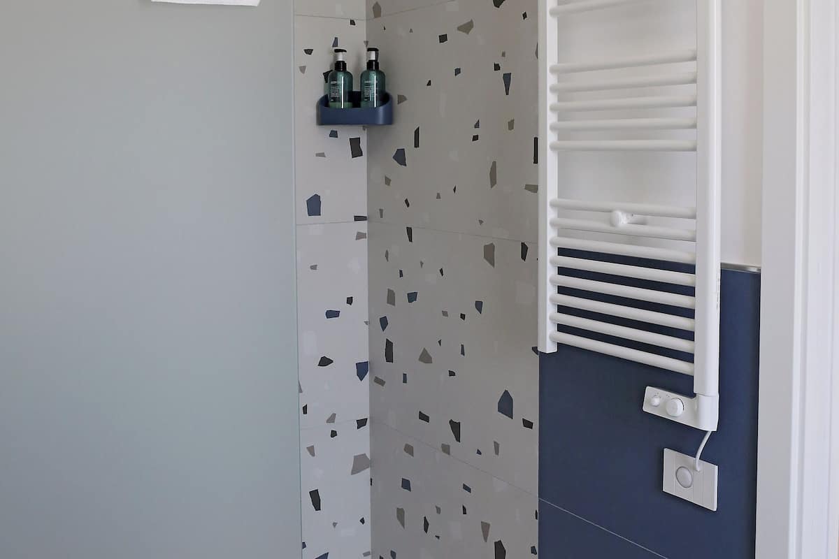 Un baño con ducha, una toalla colgada en la puerta, un estante con artículos de aseo y un perchero.
