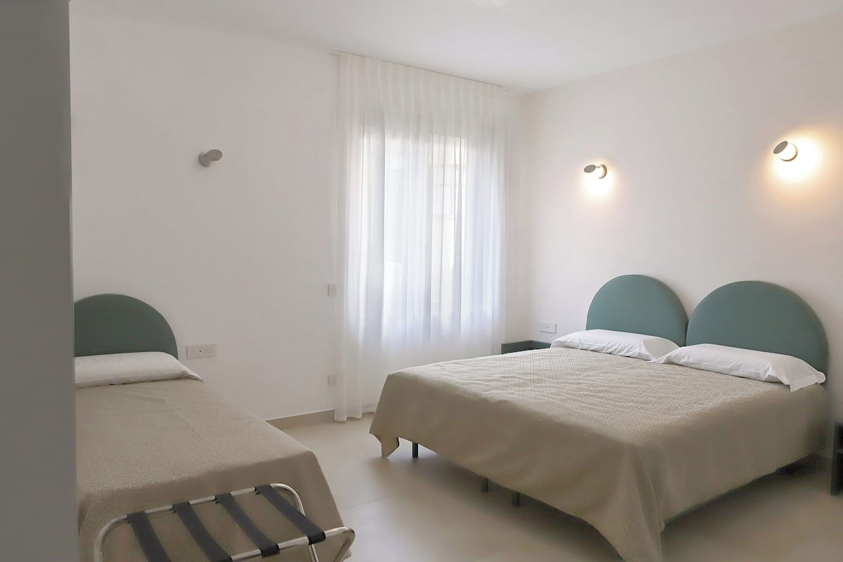 Un dormitorio con dos camas, una ventana con cortinas e iluminación en la pared.