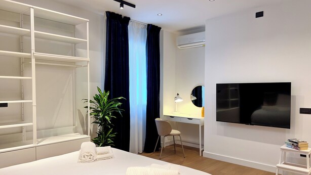 Ein Hotelzimmer mit Bett, Schreibtisch mit Stuhl, Fernseher, Pflanze und Kleiderschrank.