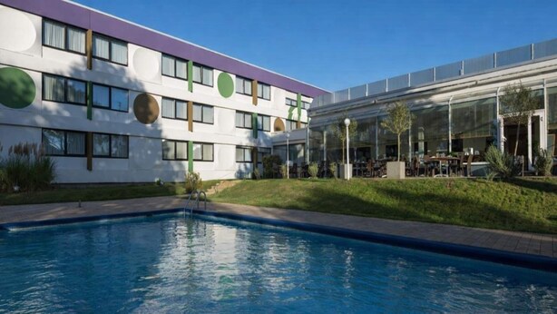 Un edificio moderno con piscina, mobiliario exterior y estructura de vidrio.
