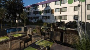 Un hotel con terraza exterior, piscina y un edificio con ventanas amplias y diseños circulares.