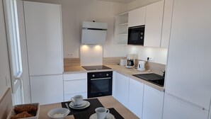 Eine kompakte Küche mit weißen Schränken, einem eingebauten Ofen, einer Mikrowelle und einer Kaffeemaschine.