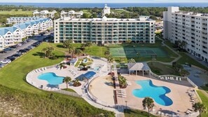 Un resort con varias piscinas, cancha de tenis y un gran edificio de hotel.