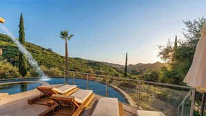 A poolside area with lounge chairs and a glass railing overlooking a mountainous landscape.