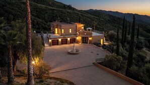 A large, two-story house with a driveway, a fountain, and a landscaped garden.