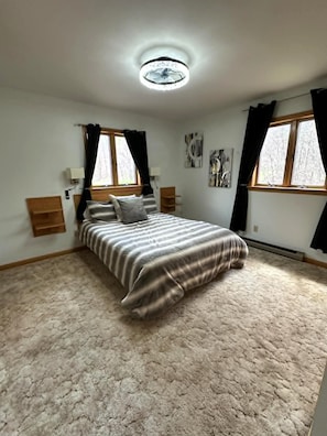 A bedroom with a bed, two bedside tables, a ceiling fan, and two windows with curtains.