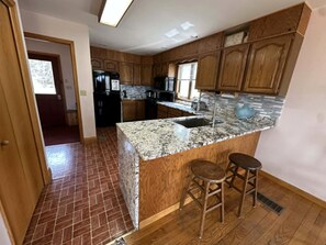 A kitchen with wooden cabinets, a granite countertop, a sink, and two stools.