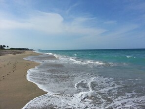 Ein Strand mit blauem Himmel, sanften Wellen und Fußabdrücken im Sand.