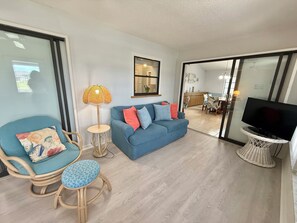 A living room with a blue sofa, a wicker chair, a small round table, a lamp, and a TV on a stand. - Sea Breeze - a perfect place for your vacation. (Port Charlotte)