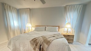Een slaapkamer met een groot bed, twee nachtkastjes met lampen en dunne gordijnen.
