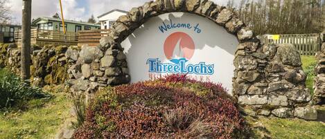 A stone archway with a welcome sign for Three Lochs Hotel Park.