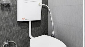 A white toilet with a tank, connected to a wall-mounted flush handle and a pipe. - Hotel Evergreen Clarks (Lucknow)