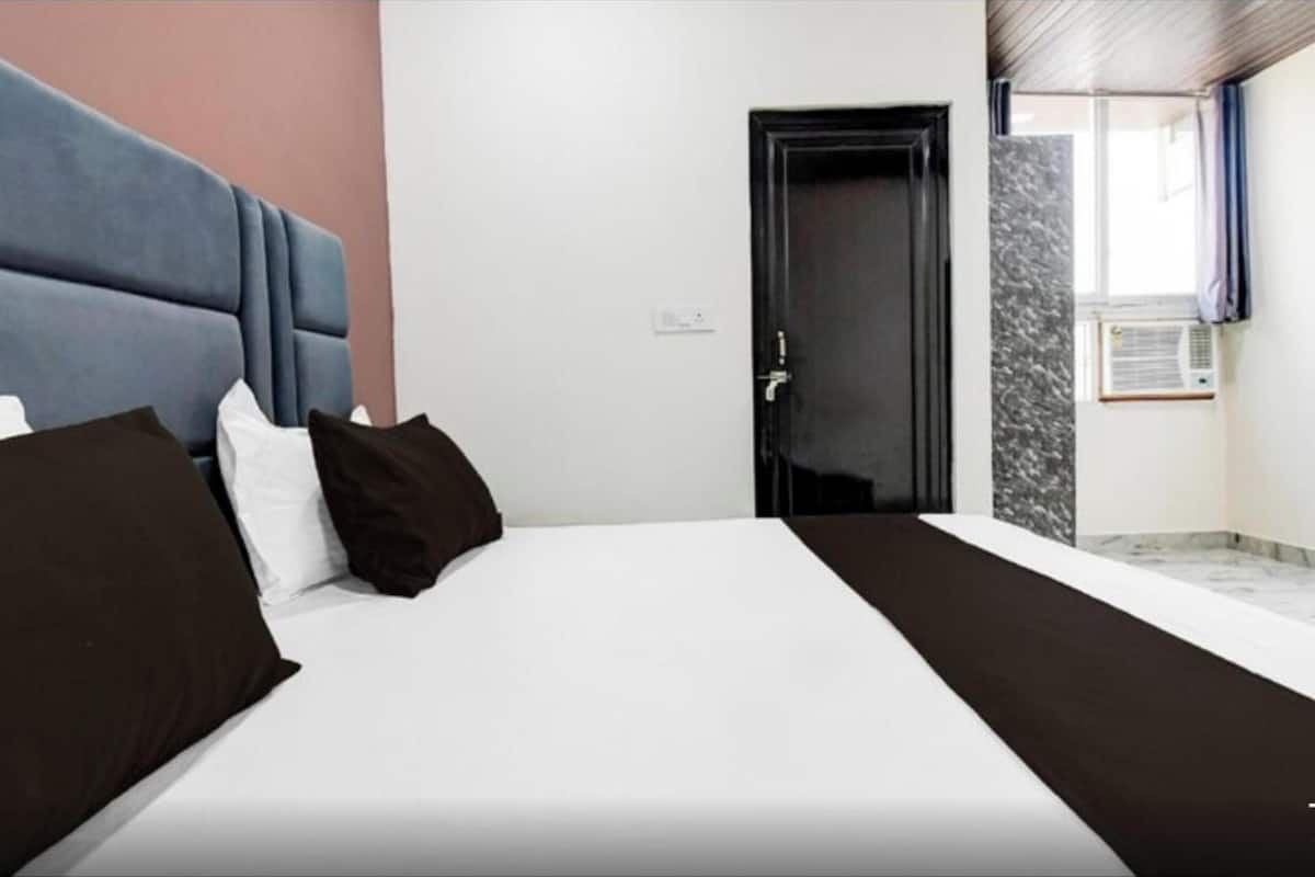 Una habitación de hotel con una cama, una puerta, una ventana y aire acondicionado instalado en la pared.