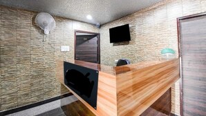 A reception area with a wooden reception desk, a wall-mounted TV, a door, and a ceiling fan. - Hotel Evergreen Clarks (Lucknow)