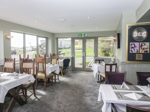Restaurante com mesas postas para refeição, cadeiras, sinal de saída de emergência e vista para o exterior.