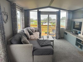 Salón con sofá, una mesita, televisor y vista a un paisaje verde.