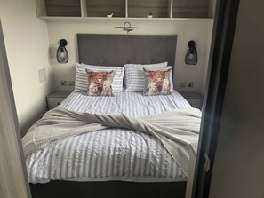 Uma cama com roupa de cama listrada, duas almofadas com estampas de animais, luminárias de cabeceira e um painel de cabeceira de design simples.