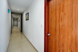 A hallway with a wooden door, white walls, and a tiled floor.