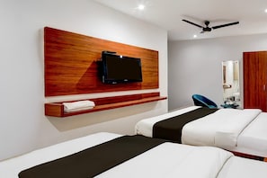 A hotel room with two beds, a mounted TV, a ceiling fan, and a wooden shelf with a towel.