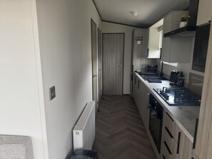 A narrow kitchen with a radiator, a stove, and a sign indicating the kitchen area. - Lochwood Platinum Superior at Three Lochs Holiday Park (Newton Stewart)